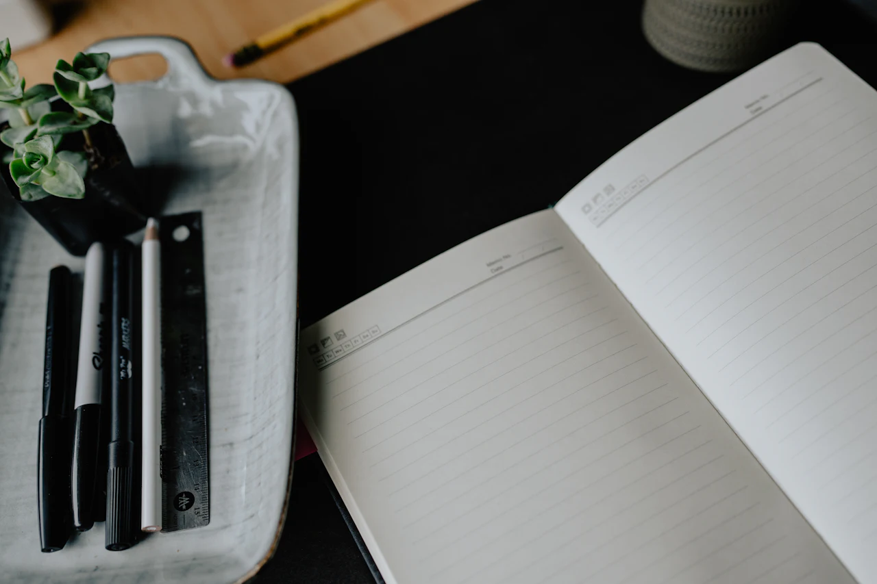 An open notebook and pens on a dark desk